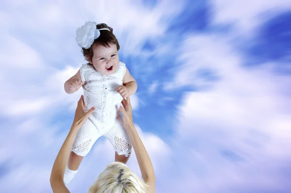 Child in white in mother hands under sky background — Stock Photo, Image