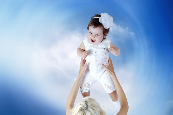 Дитина в білому в руках матері під фоном неба Стокове Зображення