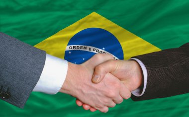 Businessmen handshake after good deal in front of brazil flag clipart