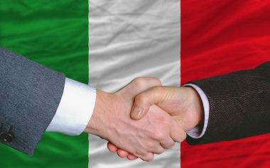 Businessmen handshake after good deal in front of italy flag clipart