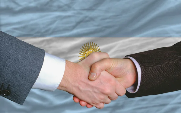 Empresários aperto de mão depois de um bom negócio na frente da bandeira argentina — Fotografia de Stock