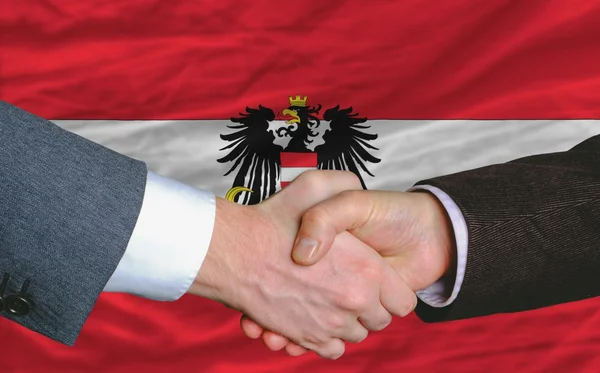 Hombres de negocios apretón de manos después de un buen trato frente a la bandera austriaca —  Fotos de Stock