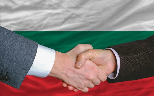 Бизнесмены пожали друг другу руки после выгодной сделки перед флагом Болгарии — стоковое фото