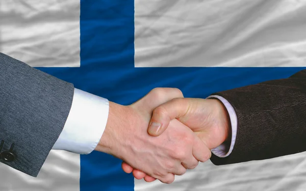 Empresários aperto de mão depois de um bom negócio na frente da bandeira da Finlândia — Fotografia de Stock