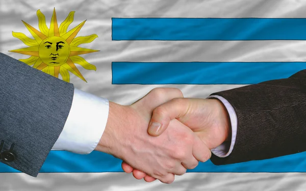 Деловые люди пожали друг другу руки после хорошей сделки перед флагом Уругвая — стоковое фото
