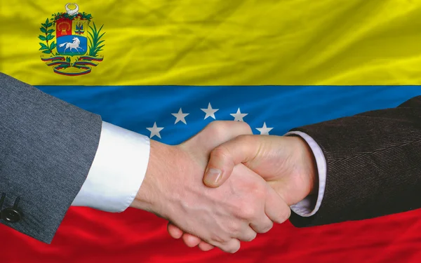 Empresários aperto de mão depois de um bom negócio na frente da bandeira venezuela — Fotografia de Stock
