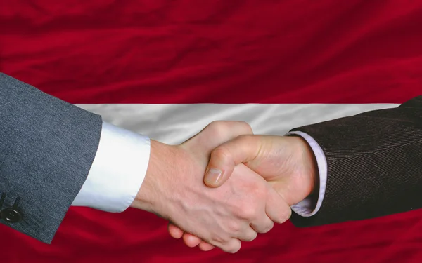 Бізнесмени рукостискання після багато перед прапор Латвії — стокове фото