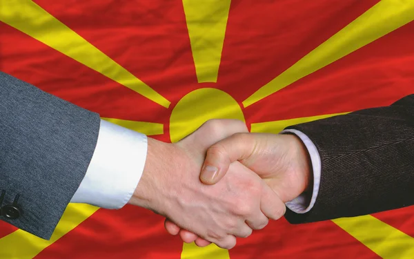 Empresários aperto de mão depois de um bom negócio na frente da bandeira macedônia — Fotografia de Stock