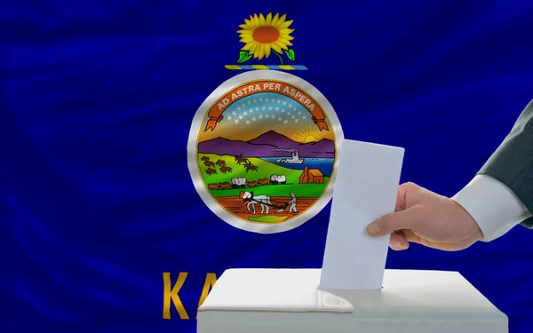Мужчина голосует на выборах перед флагом штата Канзас — стоковое фото