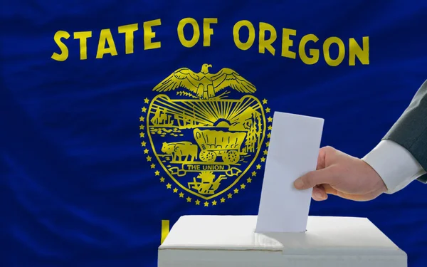 Man voting on elections in front of flag US state flag of oregon — Stock Photo, Image