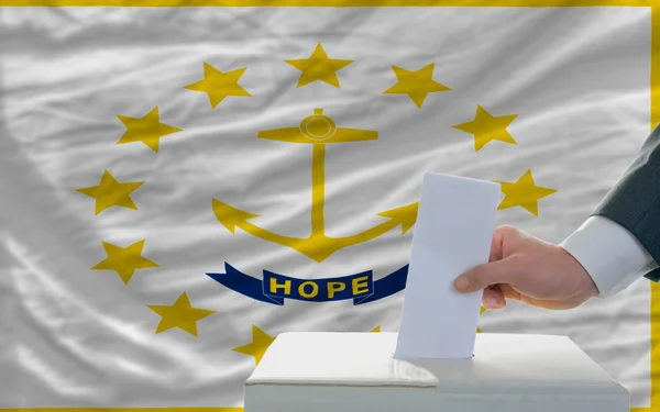 Мужчина голосует на выборах перед флагом штата Род — стоковое фото
