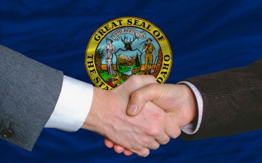 In front of american state flag of idaho two businessmen handsha clipart