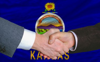 In front of american state flag of kansas two businessmen handsh clipart