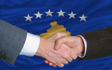 In front of flag of kosovo two businessmen handshake after good clipart