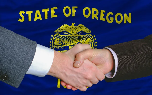 In front of american state flag of oregon two businessmen handsh — Stok fotoğraf