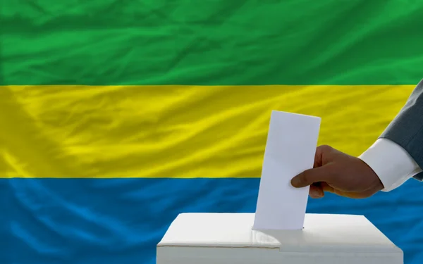 Uomo che vota per le elezioni davanti alla bandiera nazionale del Gabon — Foto Stock