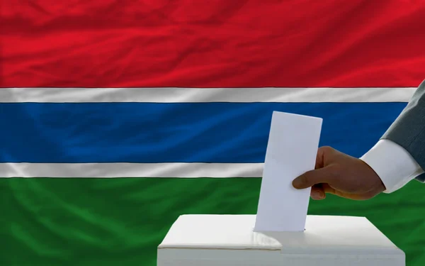 Мужчина голосует на выборах перед национальным флагом Гамбии — стоковое фото