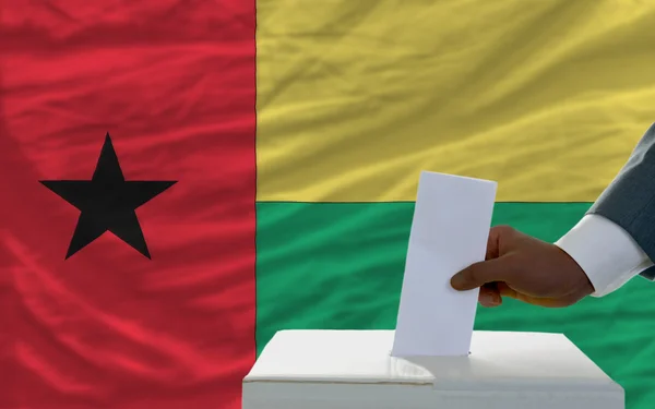 Hombre votando las elecciones frente a la bandera nacional de Guinea Biss — Foto de Stock