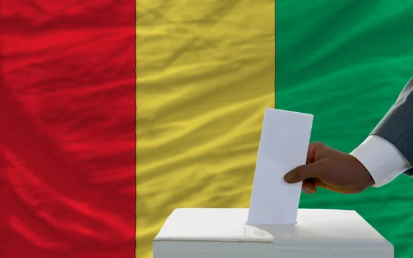 Мужчина голосует на выборах перед национальным флагом Гвинеи — стоковое фото