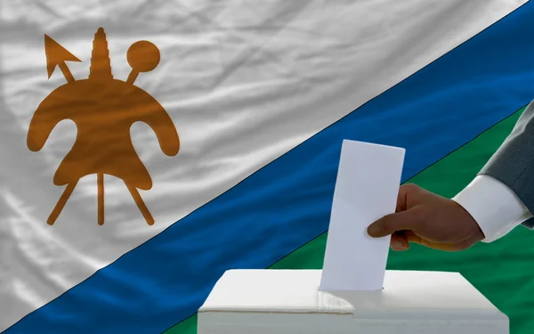 Homem votando nas eleições em frente à bandeira nacional do lesotho — Fotografia de Stock