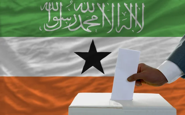 Hombre votando en elecciones frente a la bandera nacional de Somalilandia — Foto de Stock