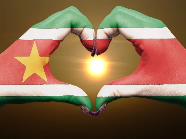 Geste de coeur et d'amour par les mains colorées dans le drapeau du Suriname pendant — Photo