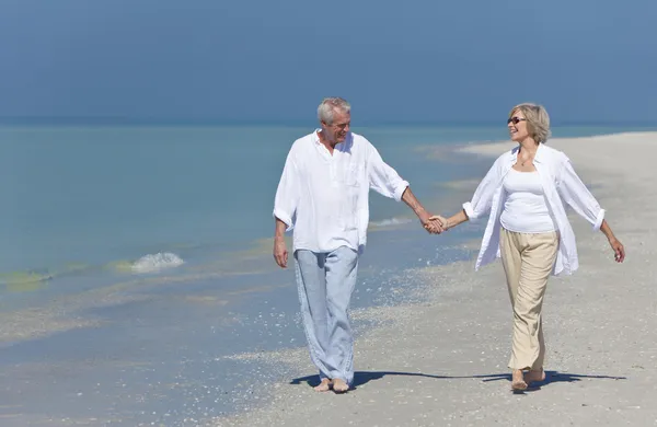 Счастливая пожилая пара гуляет, держась за руки на пляже — стоковое фото