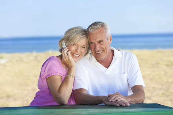 Gelukkig senior koppel met behulp van mobiele telefoon aan tafel aan strand — Stockfoto