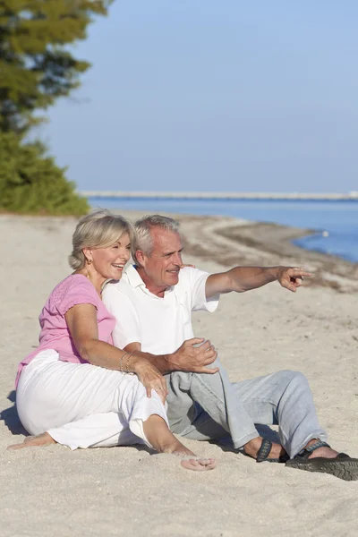 Feliz casal sênior sentado apontando na praia — Fotografia de Stock