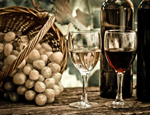 Wijnflessen, twee glazen en druiven in mand — Stockfoto