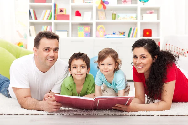 Família jovem com dois filhos lendo um livro de história — Fotografia de Stock