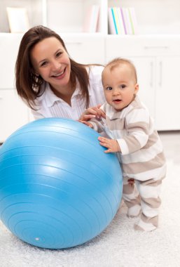 Little baby girl stands by a large exercise ball clipart