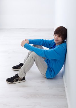 Teenager boy sitting by the wall clipart