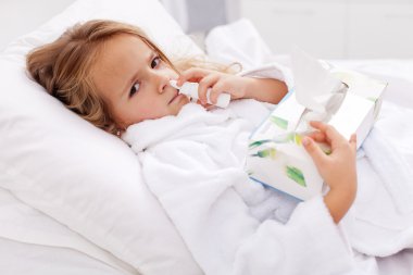 Little girl with bad cold - using nasal spray and paper napkins clipart