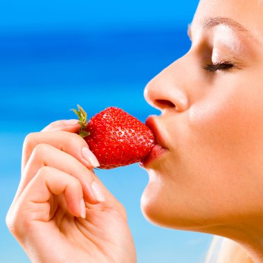 Young woman with strawberry on beach clipart