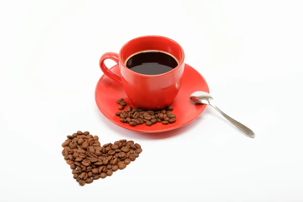 Herz aus Kaffeebohnen um eine Tasse Kaffee auf einem Tisch — Stockfoto