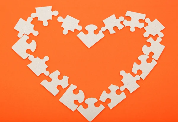 Pussel i form av ett hjärta på en orange bakgrund. — Stockfoto