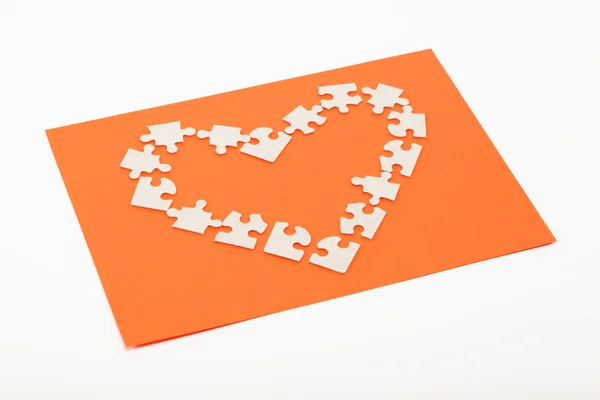Puzzles in the shape of a heart on an orange background. — Stock Photo, Image