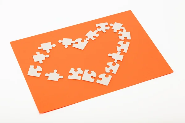 Pussel i form av ett hjärta på en orange bakgrund. — Stockfoto