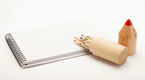 Cuaderno y lápices de colores en una caja de madera sobre un fondo blanco — Foto de Stock