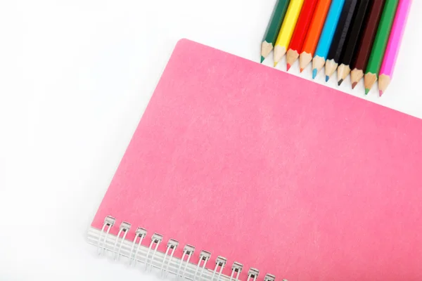 Notebook a barevné tužky na bílém pozadí. — Stock fotografie