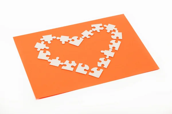 Quebra-cabeças na forma de um coração em um fundo laranja . — Fotografia de Stock