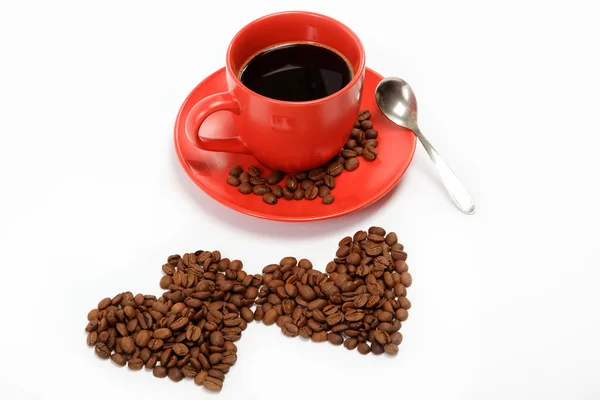 Herz aus Kaffeebohnen um eine Tasse Kaffee auf einem Tisch — Stockfoto