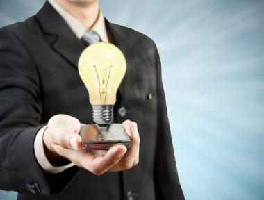 Businessman holding mobile phone light bulb coming out technolo clipart