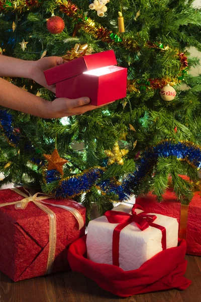 Human hand holding open gift on christmas tree background — Stock Photo, Image