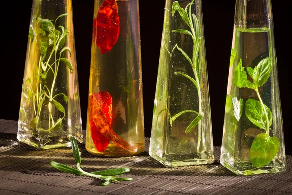 Vier Flaschen mit Pflanzenöl und frischen Gewürzen — Stockfoto