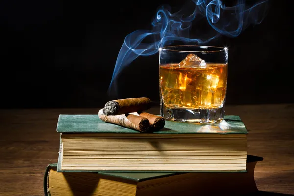 Sigaar met blauwe rook en whisky op ijs en twee boeken volume — Stockfoto