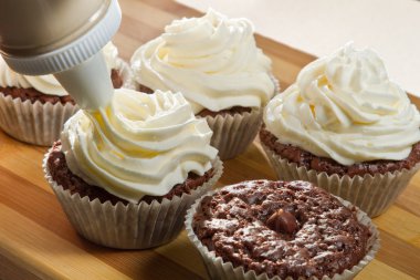 Decorating chocolate muffin with vanilla cream clipart