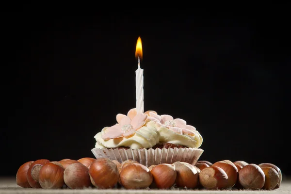 Muffin with small burning candle and huzelnuts — Stock Photo, Image