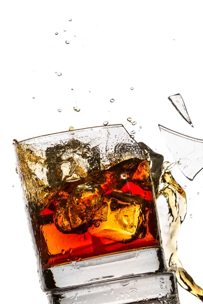 Ice cubes breaking whisky glass filled with bourbon on white bac — Stock Photo, Image